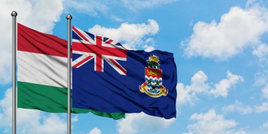 Macaristan ve Cayman Adaları bayrağı birlikte beyaz bulutlu mavi gökyüzüne karşı rüzgarsal sallayarak. Diplomasi kavramı, uluslararası ilişkiler.