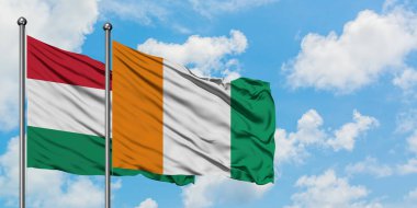 Macaristan ve Fildişi Sahili bayrağı birlikte beyaz bulutlu mavi gökyüzüne karşı rüzgarda sallayarak. Diplomasi kavramı, uluslararası ilişkiler.