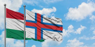 Macaristan ve Faroe Adaları bayrağı birlikte beyaz bulutlu mavi gökyüzüne karşı rüzgarda sallayarak. Diplomasi kavramı, uluslararası ilişkiler.