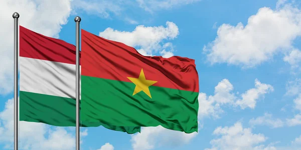 Bandera de Hungría y Burkina Faso ondeando en el viento contra el cielo azul nublado blanco juntos. Concepto diplomático, relaciones internacionales . — Foto de Stock
