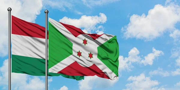 Bandera de Hungría y Burundi ondeando en el viento contra el cielo azul nublado blanco juntos. Concepto diplomático, relaciones internacionales . — Foto de Stock