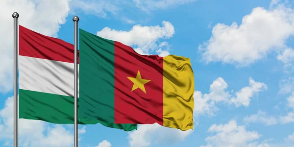 Bandera de Hungría y Camerún ondeando en el viento contra el cielo azul nublado blanco juntos. Concepto diplomático, relaciones internacionales . — Foto de Stock