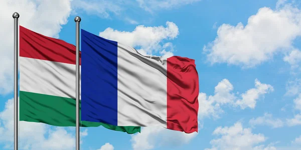 Bandera de Hungría y Francia ondeando en el viento contra el cielo azul nublado blanco juntos. Concepto diplomático, relaciones internacionales . — Foto de Stock