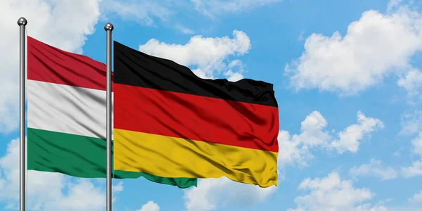 Bandera de Hungría y Alemania ondeando en el viento contra el cielo azul nublado blanco juntos. Concepto diplomático, relaciones internacionales . — Foto de Stock