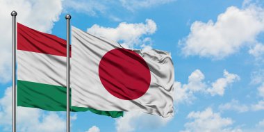 Macaristan ve Japonya bayrağı birlikte beyaz bulutlu mavi gökyüzüne karşı rüzgarda sallayarak. Diplomasi kavramı, uluslararası ilişkiler.