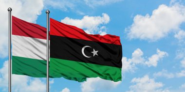 Macaristan ve Libya bayrağı birlikte beyaz bulutlu mavi gökyüzüne karşı rüzgarsal sallayarak. Diplomasi kavramı, uluslararası ilişkiler.