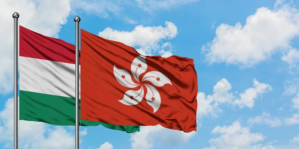 Bandera de Hungría y Hong Kong ondeando en el viento contra el cielo azul nublado blanco juntos. Concepto diplomático, relaciones internacionales . — Foto de Stock