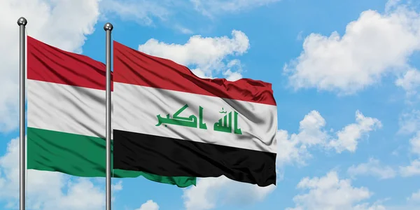 A Hungria e a bandeira do Iraque agitando no vento contra o céu azul nublado branco juntos. Conceito de diplomacia, relações internacionais . — Fotografia de Stock