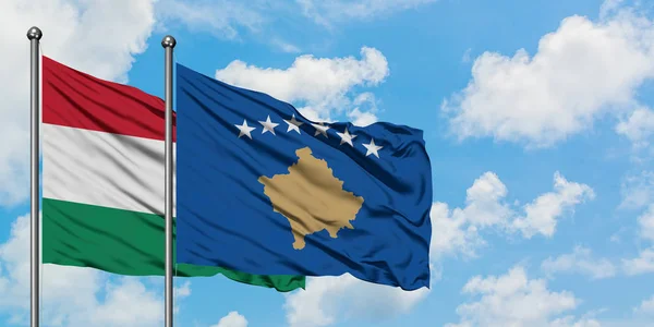 Bandera de Hungría y Kosovo ondeando en el viento contra el cielo azul nublado blanco juntos. Concepto diplomático, relaciones internacionales . — Foto de Stock