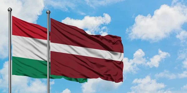 Bandera de Hungría y Letonia ondeando en el viento contra el cielo azul nublado blanco juntos. Concepto diplomático, relaciones internacionales . — Foto de Stock