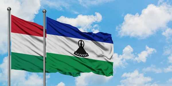 Bandera de Hungría y Lesotho ondeando en el viento contra el cielo azul nublado blanco juntos. Concepto diplomático, relaciones internacionales . — Foto de Stock