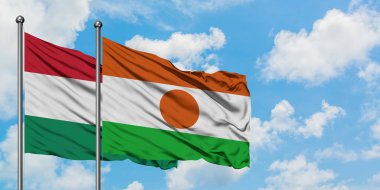 Macaristan ve Nijer bayrağı birlikte beyaz bulutlu mavi gökyüzüne karşı rüzgarda sallayarak. Diplomasi kavramı, uluslararası ilişkiler.