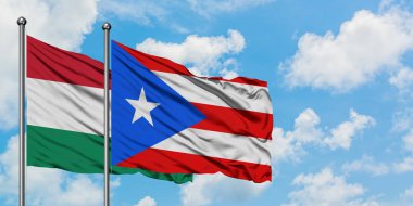 Macaristan ve Porto Riko bayrağı birlikte beyaz bulutlu mavi gökyüzüne karşı rüzgarda sallayarak. Diplomasi kavramı, uluslararası ilişkiler.