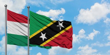 Macaristan ve Saint Kitts ve Nevis bayrağı birlikte beyaz bulutlu mavi gökyüzüne karşı rüzgarda sallayarak. Diplomasi kavramı, uluslararası ilişkiler.