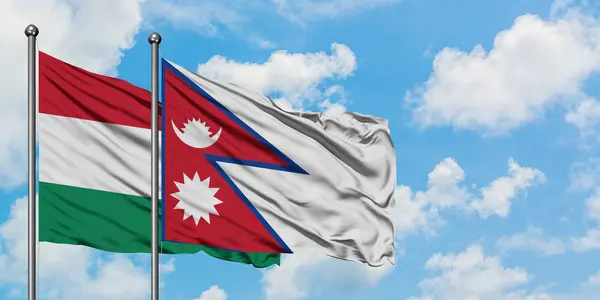 Bandera de Hungría y Nepal ondeando en el viento contra el cielo azul nublado blanco juntos. Concepto diplomático, relaciones internacionales . — Foto de Stock