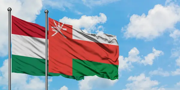 Bandera de Hungría y Omán ondeando en el viento contra el cielo azul nublado blanco juntos. Concepto diplomático, relaciones internacionales . — Foto de Stock