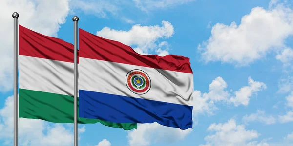 Bandera de Hungría y Paraguay ondeando en el viento contra el cielo azul nublado blanco juntos. Concepto diplomático, relaciones internacionales . — Foto de Stock