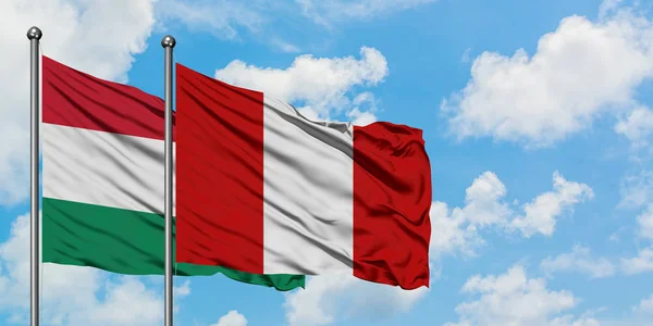 Bandera de Hungría y Perú ondeando en el viento contra el cielo azul nublado blanco juntos. Concepto diplomático, relaciones internacionales . — Foto de Stock