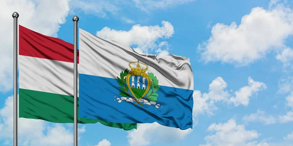 Bandera de Hungría y San Marino ondeando en el viento contra el cielo azul nublado blanco juntos. Concepto diplomático, relaciones internacionales . — Foto de Stock