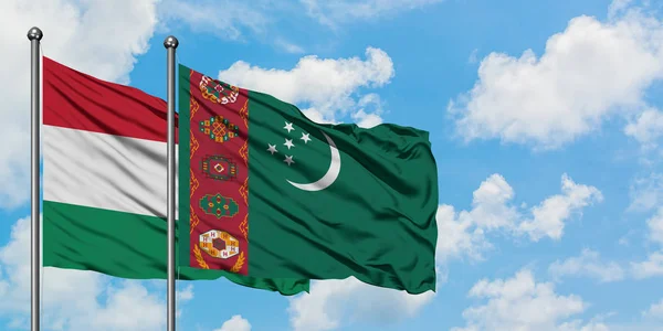 Bandera de Hungría y Turkmenistán ondeando en el viento contra el cielo azul nublado blanco juntos. Concepto diplomático, relaciones internacionales . — Foto de Stock