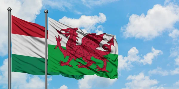 A bandeira da Hungria e do País de Gales agitando no vento contra o céu azul nublado branco juntos. Conceito de diplomacia, relações internacionais . — Fotografia de Stock