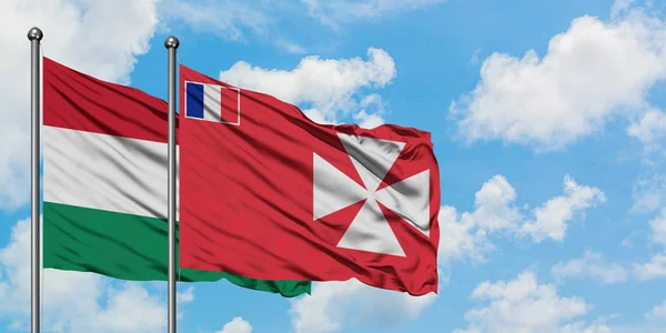 Maďarsko a Wallis a Futuna vlají ve větru proti bíle zatažené modré obloze. Diplomacie, mezinárodní vztahy. — Stock fotografie