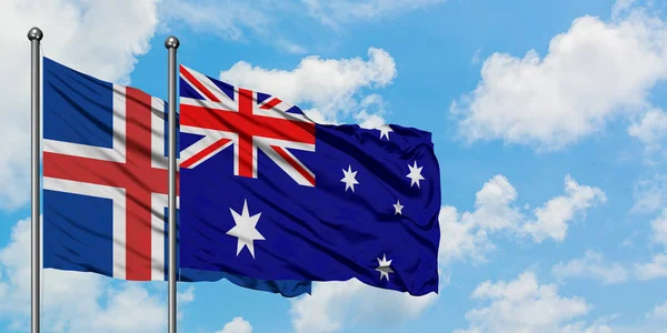 Island- und Australienfahne wehen gemeinsam im Wind gegen den wolkenverhangenen blauen Himmel. Diplomatie-Konzept, internationale Beziehungen. — Stockfoto