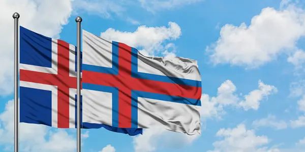Bandera de Islandia y las Islas Feroe ondeando en el viento contra el cielo azul nublado blanco juntos. Concepto diplomático, relaciones internacionales . — Foto de Stock