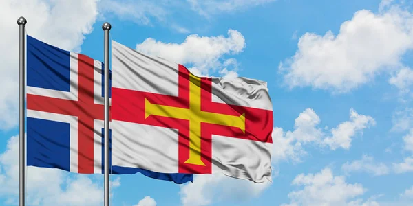 Islândia e Guernsey bandeira acenando no vento contra o céu azul nublado branco juntos. Conceito de diplomacia, relações internacionais . — Fotografia de Stock