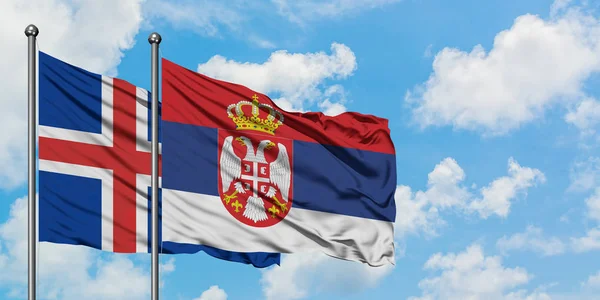 Bandera de Islandia y Serbia ondeando en el viento contra el cielo azul nublado blanco juntos. Concepto diplomático, relaciones internacionales . — Foto de Stock