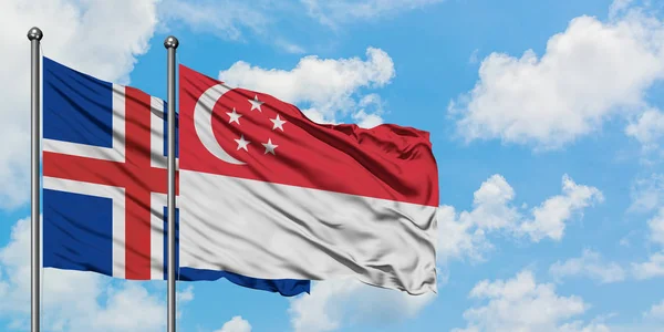 Island- und Singapore-Flagge wehen gemeinsam im Wind gegen den wolkenverhangenen blauen Himmel. Diplomatie-Konzept, internationale Beziehungen. — Stockfoto