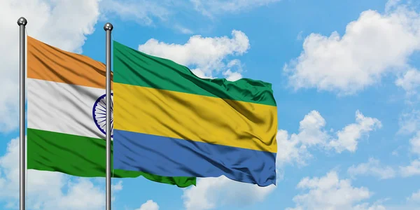 Bandera de India y Gabón ondeando en el viento contra el cielo azul nublado blanco juntos. Concepto diplomático, relaciones internacionales . — Foto de Stock