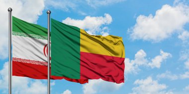 İran ve Benin bayrağı birlikte beyaz bulutlu mavi gökyüzüne karşı rüzgarsal sallayarak. Diplomasi kavramı, uluslararası ilişkiler.