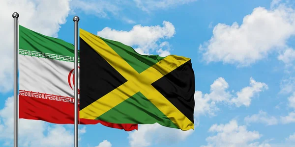Bandera de Irán y Jamaica ondeando en el viento contra el cielo azul nublado blanco juntos. Concepto diplomático, relaciones internacionales . — Foto de Stock