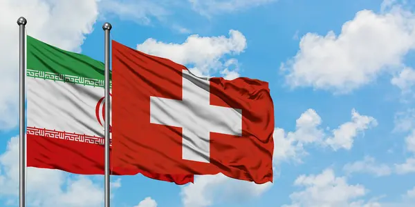 Írán a Švýcarsko vlaje ve větru proti bíle zatažené modré obloze. Diplomacie, mezinárodní vztahy. — Stock fotografie