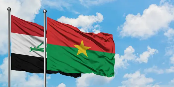 Bandera de Irak y Burkina Faso ondeando en el viento contra el cielo azul nublado blanco juntos. Concepto diplomático, relaciones internacionales . — Foto de Stock