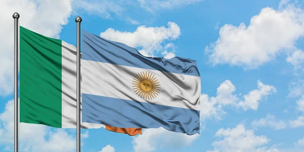 Bandera de Irlanda y Argentina ondeando en el viento contra el cielo azul nublado blanco juntos. Concepto diplomático, relaciones internacionales . — Foto de Stock