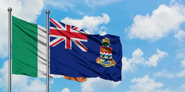 Bandera de Irlanda y las Islas Caimán ondeando en el viento contra el cielo azul nublado blanco juntos. Concepto diplomático, relaciones internacionales . — Foto de Stock