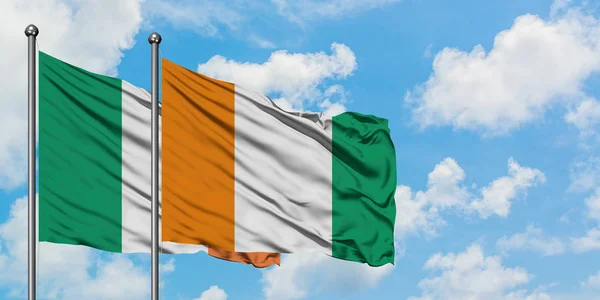 Irlanda e Costa d'Avorio sventolano insieme la bandiera contro il bianco cielo azzurro nuvoloso. Concetto di diplomazia, relazioni internazionali . — Foto Stock