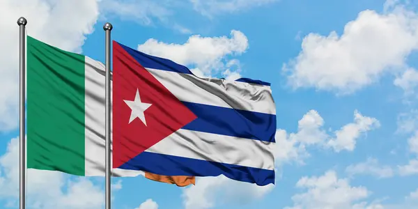 Irská a Kubánská vlajka mávajících větrem proti bílé zamračené modré obloze. Diplomacie, mezinárodní vztahy. — Stock fotografie