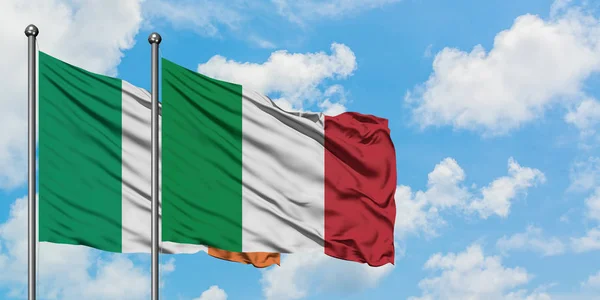 Bandera de Irlanda e Italia ondeando en el viento contra el cielo azul nublado blanco juntos. Concepto diplomático, relaciones internacionales . — Foto de Stock