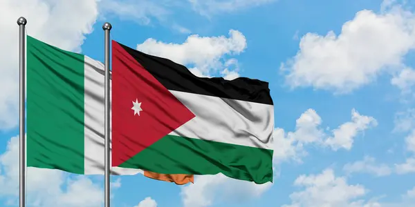 Bandera de Irlanda y Jordania ondeando en el viento contra el cielo azul nublado blanco juntos. Concepto diplomático, relaciones internacionales . — Foto de Stock