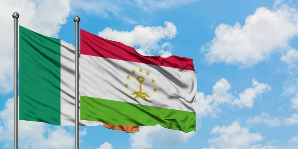 Bandera de Irlanda y Tayikistán ondeando en el viento contra el cielo azul nublado blanco juntos. Concepto diplomático, relaciones internacionales . — Foto de Stock