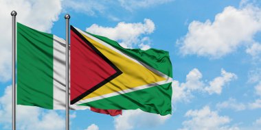 İtalya ve Guyana bayrağı birlikte beyaz bulutlu mavi gökyüzüne karşı rüzgarda sallayarak. Diplomasi kavramı, uluslararası ilişkiler.