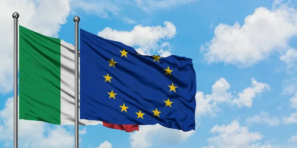 Bandera de Italia y la Unión Europea ondeando en el viento contra el cielo azul nublado blanco juntos. Concepto diplomático, relaciones internacionales . — Foto de Stock