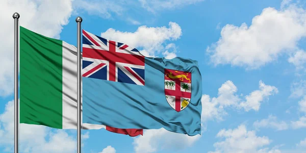 Bandera de Italia y Fiyi ondeando en el viento contra el cielo azul nublado blanco juntos. Concepto diplomático, relaciones internacionales . — Foto de Stock