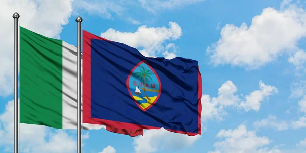 Bandera de Italia y Guam ondeando en el viento contra el cielo azul nublado blanco juntos. Concepto diplomático, relaciones internacionales . — Foto de Stock