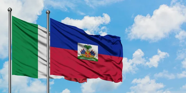 Bandera de Italia y Haití ondeando en el viento contra el cielo azul nublado blanco juntos. Concepto diplomático, relaciones internacionales . — Foto de Stock