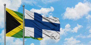 Jamaika ve Finlandiya bayrağı birlikte beyaz bulutlu mavi gökyüzüne karşı rüzgarda sallayarak. Diplomasi kavramı, uluslararası ilişkiler.