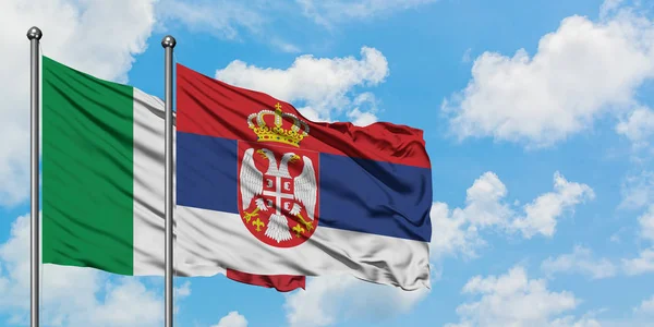 Bandera de Italia y Serbia ondeando en el viento contra el cielo azul nublado blanco juntos. Concepto diplomático, relaciones internacionales . — Foto de Stock
